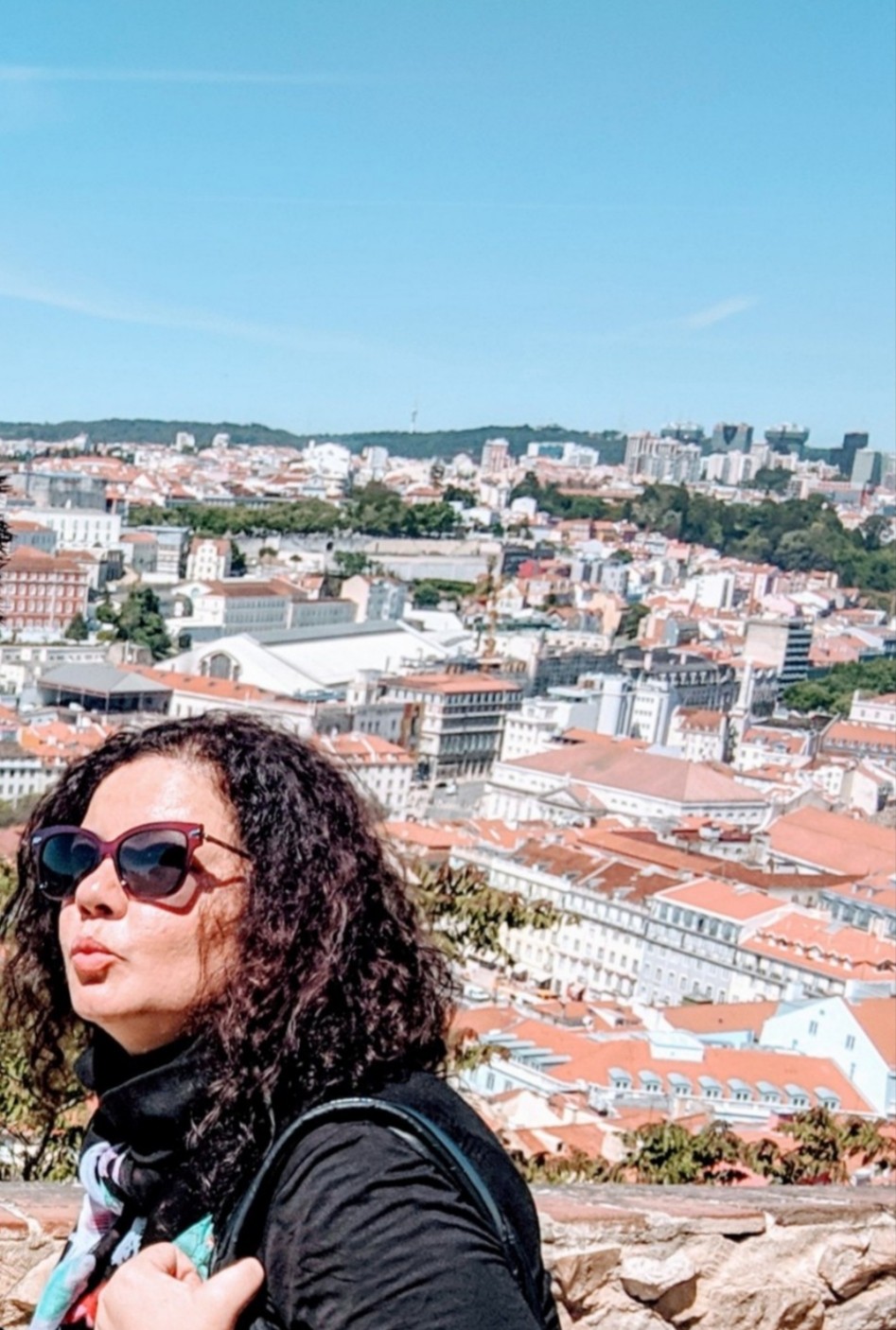 A picture of Solange Isaacs standing against a backdrop of vibrant Lisbon. She is smiling, capturing the essence of her enjoyment and wanderlust in this scenic city.