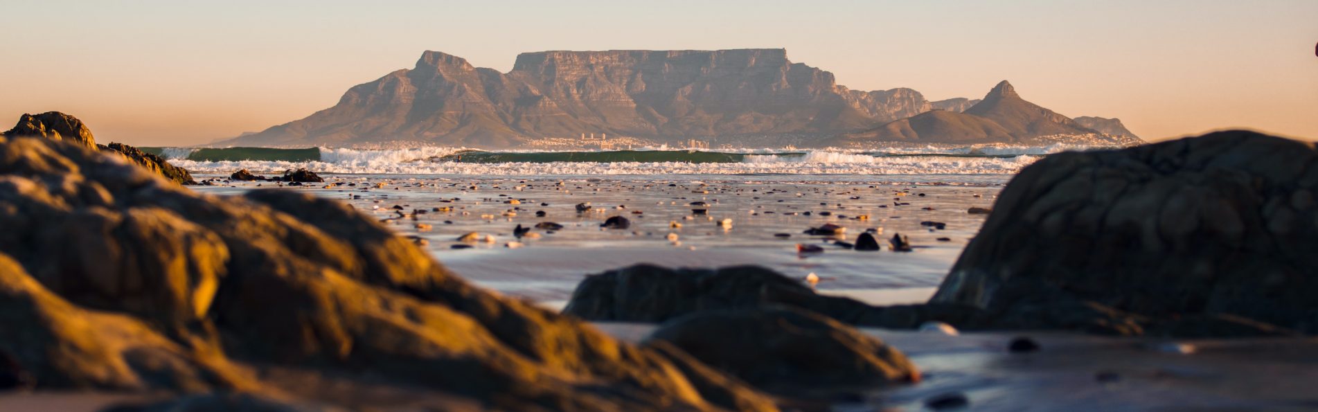 A serene beach scene in Cape Town, with golden sand, clear blue waters, and a stunning backdrop of mountains.