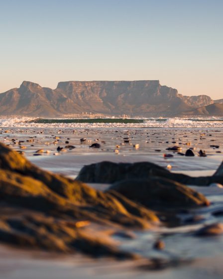 A serene beach scene in Cape Town, with golden sand, clear blue waters, and a stunning backdrop of mountains.