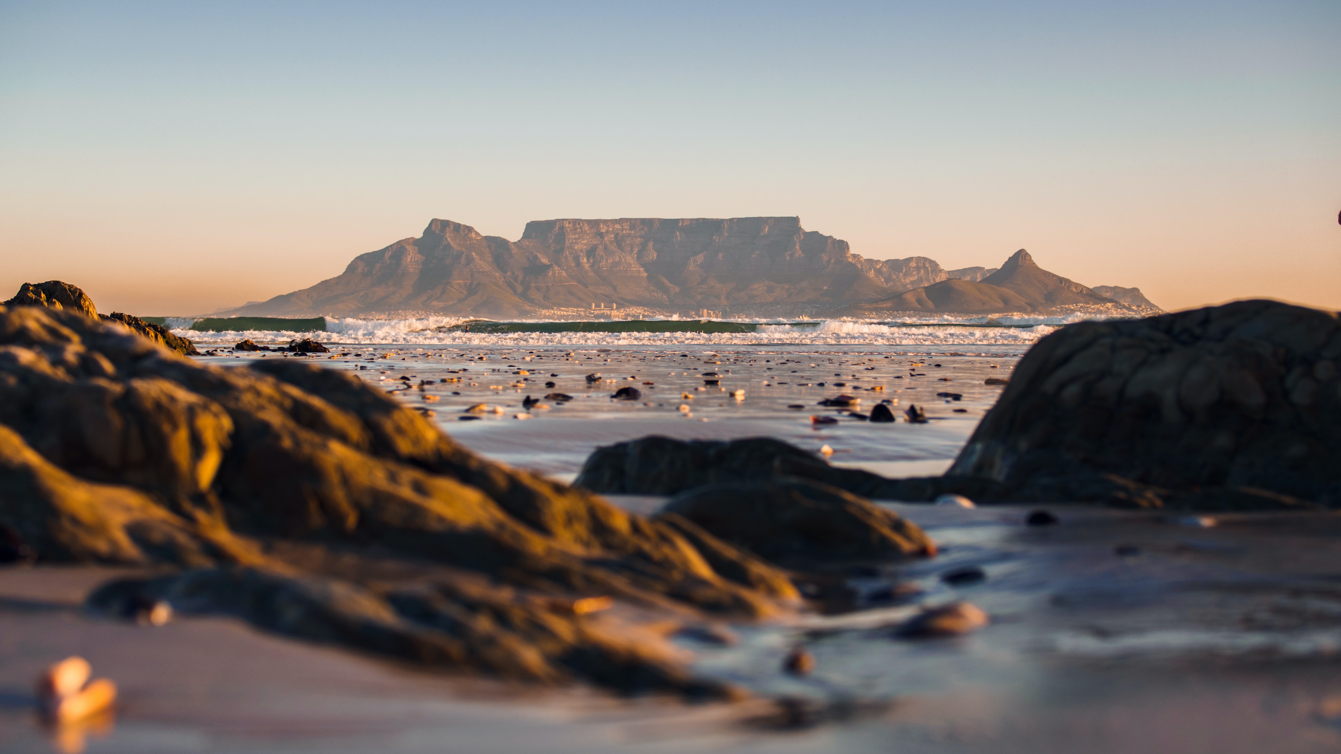 A serene beach scene in Cape Town, with golden sand, clear blue waters, and a stunning backdrop of mountains.