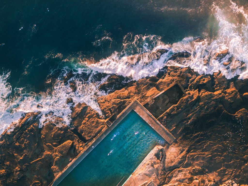 A view of the Bondi Beach Iceberg Pool nestled along the coastline, with the sparkling blue ocean in the background. 24-Hour in Sydney. Here, There, And Everywhere. Solange Isaacs.