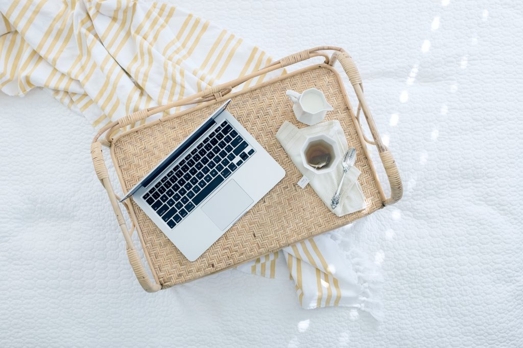 Laptop on tray with tea on bed, representing remote work and digital nomad lifestyle.