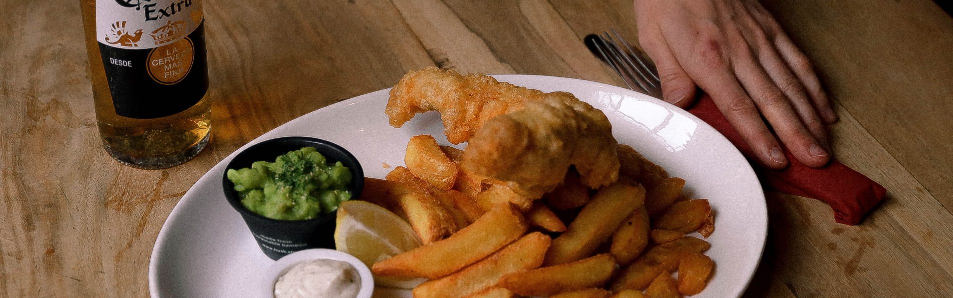 A plate of golden-brown fish fillets and crispy chips, served with tartar sauce and parsley. Here, There, And Everywhere.