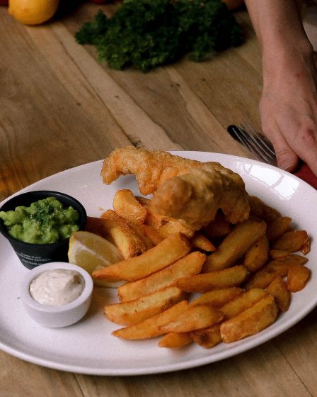 A plate of golden-brown fish fillets and crispy chips, served with tartar sauce and parsley. Here, There, And Everywhere.