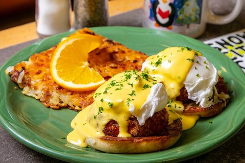 A mouthwatering egg sandwich with a golden-brown toasted bun, filled with fluffy scrambled eggs, melted cheese, crispy bacon, and fresh lettuce, served with a side of crispy hash browns.